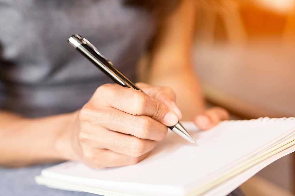 Hands write in a notebook with a pen.